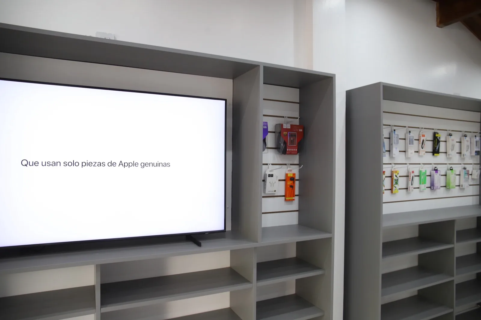 La pantalla del salón de iMasters Store, con el texto «Que usan solo piezas de Apple genuinas», junto a la pared de accesorios